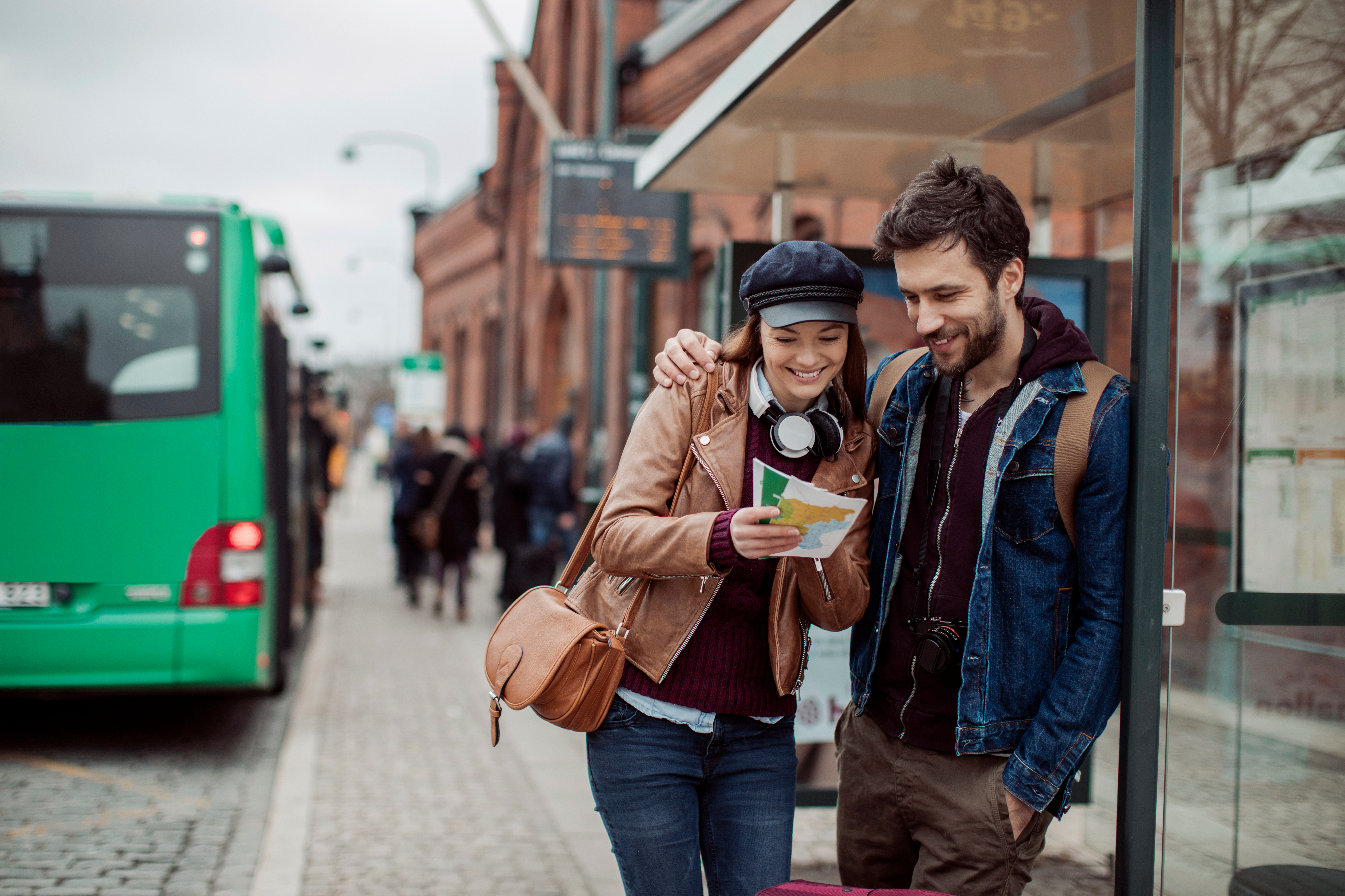 Man och kvinna står på en busstation, tittar på en karta och ler